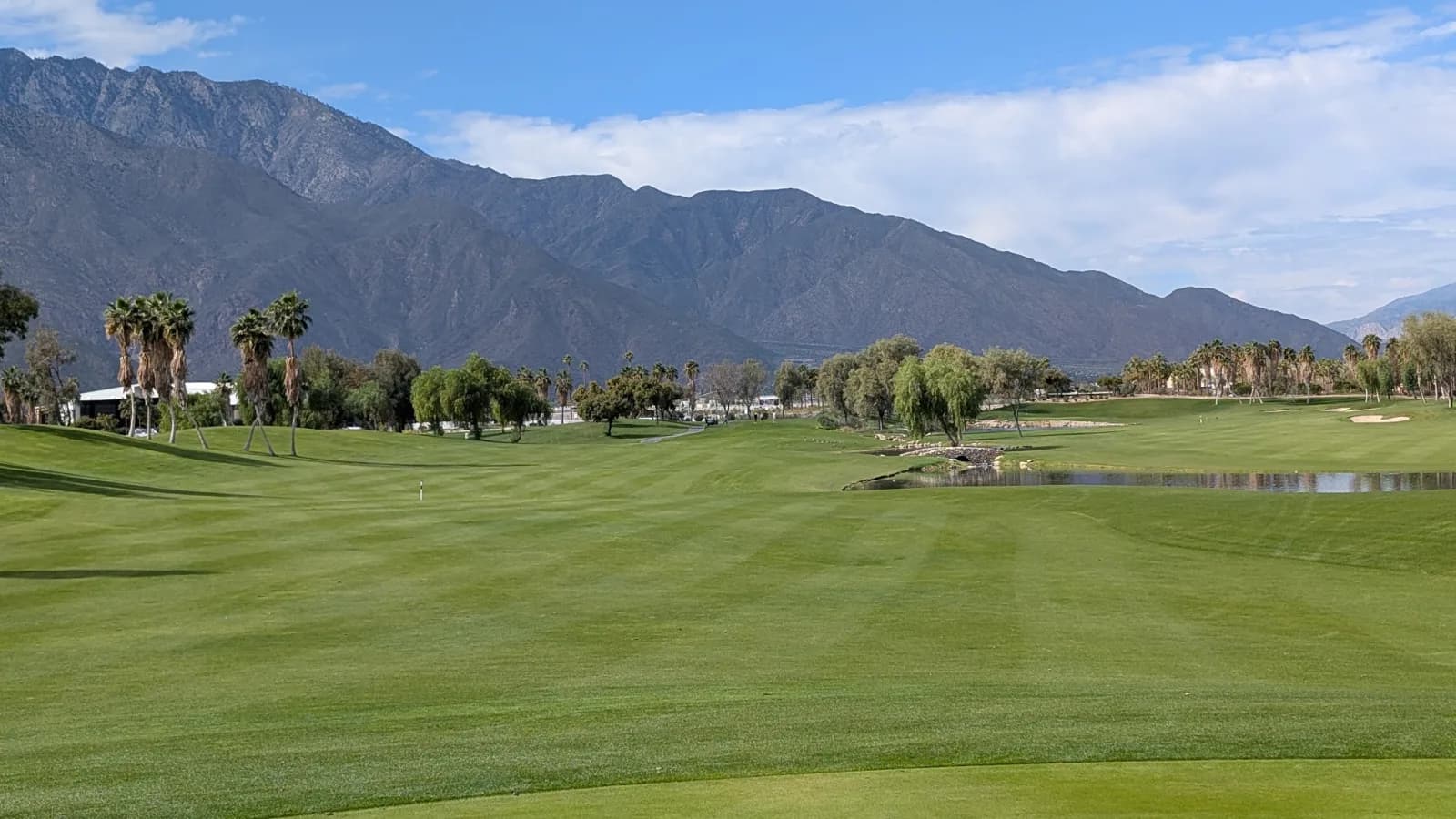 One of Escena's wide fairways, freshly striped, with a rock-edged pond on the right and a long mountain ridge across the back.