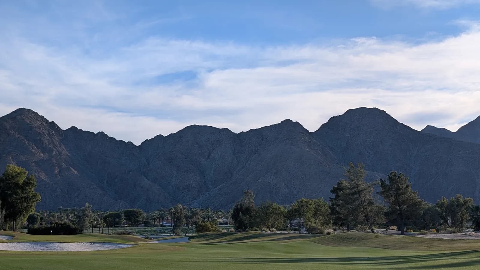 A mown Indian Wells fairway with a bunker on the left, backed by a steep dark mountain wall that fills most of the frame.