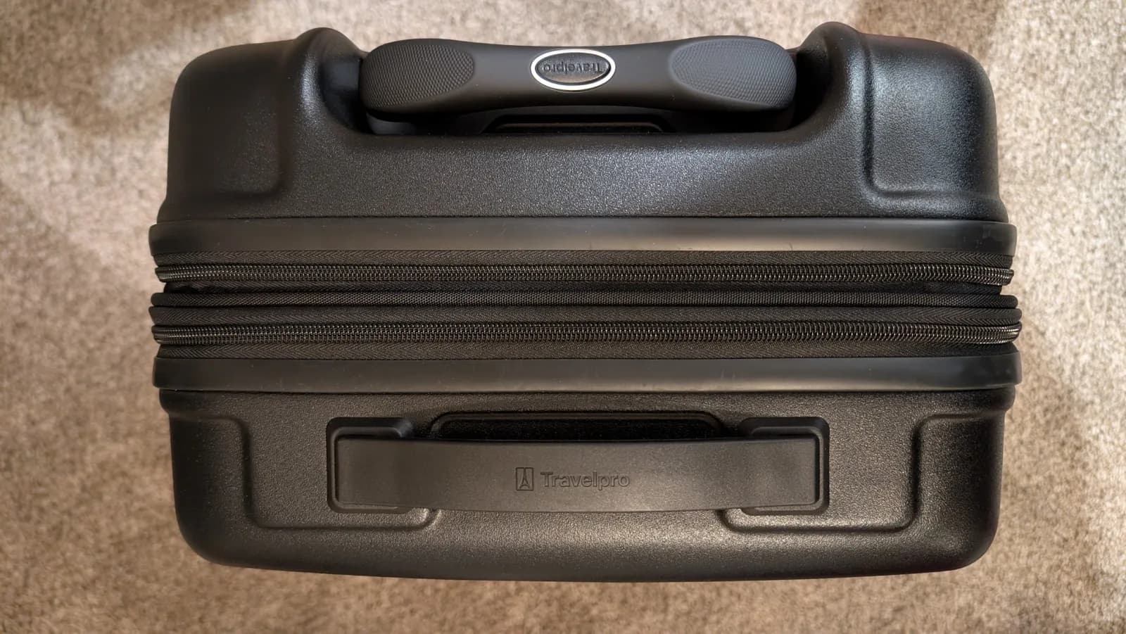 The closed bag seen from above: the telescoping handle grip running along one edge, the clamshell zipper seam across the middle, and the recessed top carry handle set into the opposite half of the case.